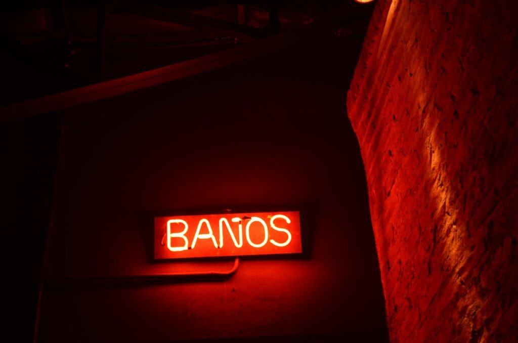 A red neon 'Baños' sign illuminates a brick wall in Buenos Aires at night.